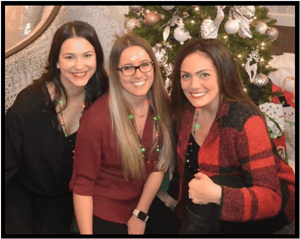 Three women in festive attire smiling near a Christmas tree for St Charles Plastic Surgery's summer newsletter.