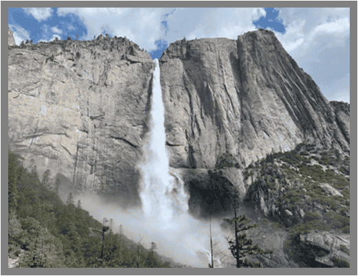Waterfall cascading from a rocky cliff near St Charles Plastic Surgery, with green vegetation and mountains.