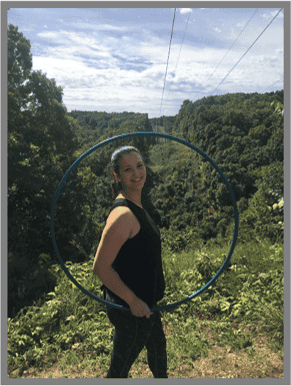 Woman joyfully holding a hula hoop in a lush landscape, representing leisure and freedom near St Charles Plastic Surgery.