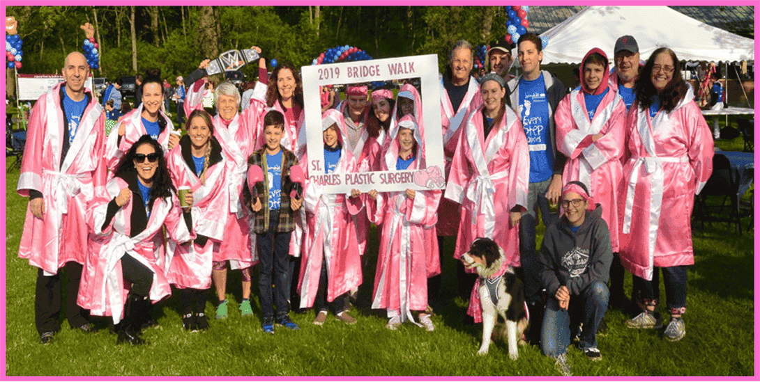 Group of people in pink robes at St Charles Plastic Surgery's 2019 Bridge Walk, featuring children, adults, and a dog.